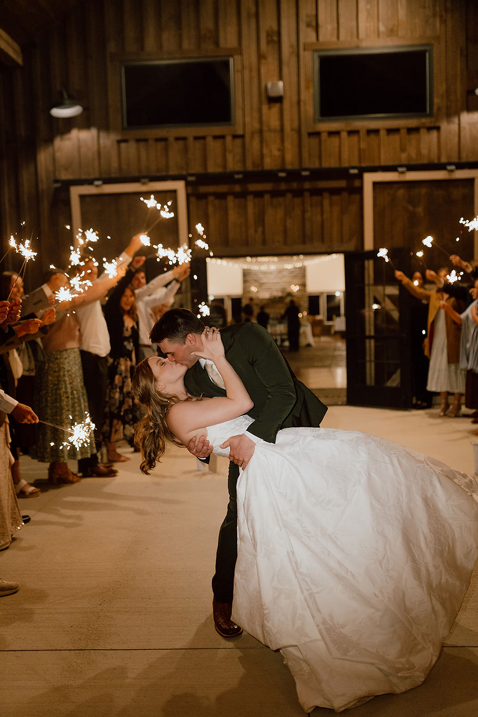 Central Ohio Wedding Venue Bride and groom kiss in a rustic barn aisle as guests hold sparklers, warm lights glowing around them.