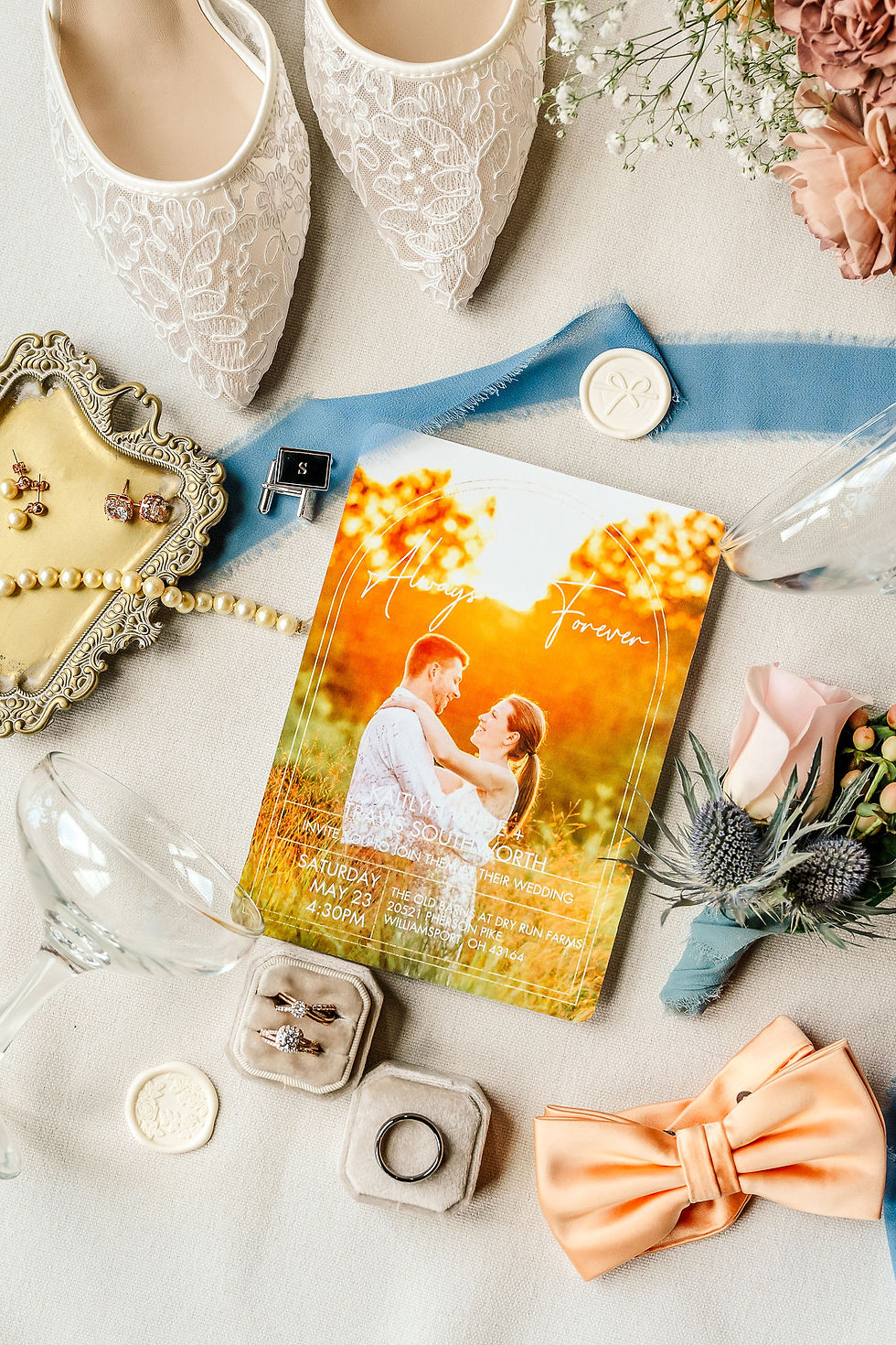 Grove City, OH Wedding Venue Wedding flat lay with lace heels, rings, flowers, and orange invite reading Always Forever on a cream fabric background.