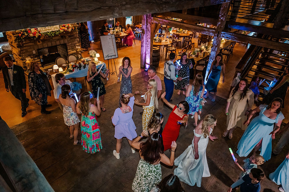 Barn Wedding Venues in Ohio. People dancing joyfully at a rustic indoor party, wearing colorful outfits. The background shows tables and a decorated fireplace.