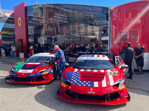 Two GT race cars positioned in front of the team’s hospitality area at a motorsport paddock, surrounded by team members and technical staff preparing for the event.
