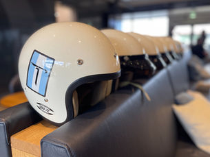 Row of white motorcycle helmets neatly lined up on a sofa, ready for use at a motorsport event.
