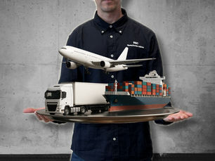 Man standing in a dark blue R&C Sports Events Logistics shirt, holding a tray with a truck, airplane, and cargo ship, symbolizing the main modes of transport in logistics: road, air, and sea.