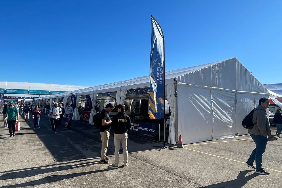 Large event tents set up along a paddock area, with teams, staff, and visitors walking under clear blue skies.