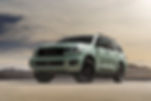 A green Toyota SUV parked on a desert road with mountains in the background under a cloudy sky, conveying a sense of adventure.