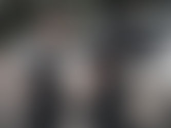 Police officer detains handcuffed person by white car in a wooded area. Officer wearing vest marked "POLICE" with hand on detainee's back. Arrested for Resting police without violence