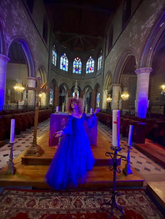 Maria Déssart vêtue d'une longue robe bleue chantant au milieu d'un chœur d'église illuminé pour le spectacle Classique 2.0 de l'agence Impulsion