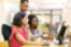 A group of young teachers sit at a computer station in an elementary school library
