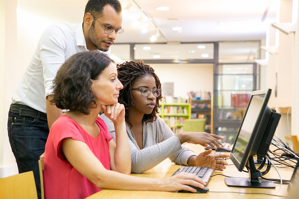A group of young teachers sit at a computer station in an elementary school library