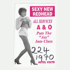 Scan of a white business card printed in pink ink with a greyscale photo of a person lifting up their shirt to reveal a bra. The text reads "Sexy New Redhead" "All Services" "A&O" "Puts the "Ass" into Class" "Hotel Visits," and a handwritten phone number.
