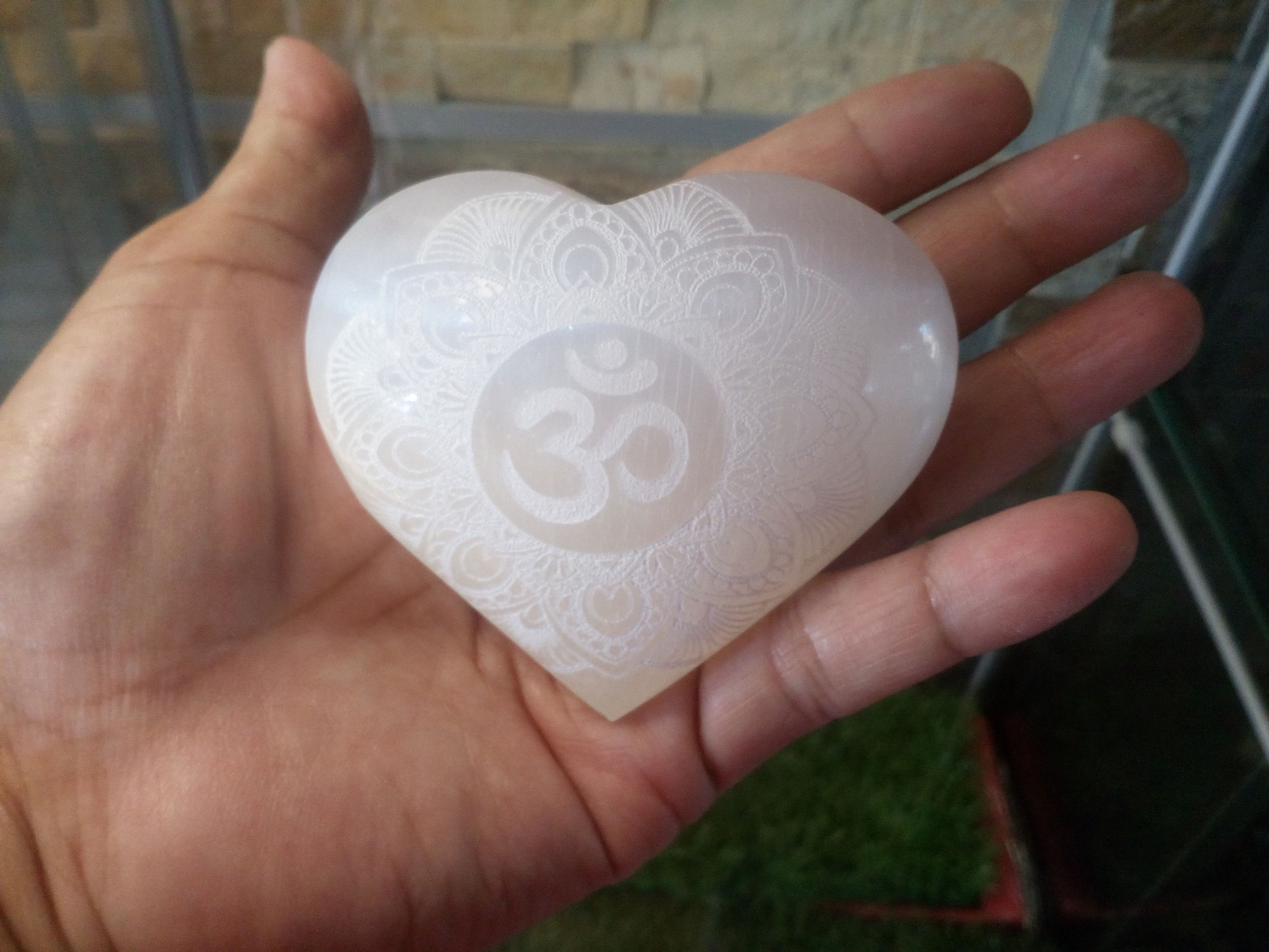 Hand holding heart-shaped Selenite crystal with Om symbol