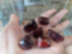 Hand holding six tumbled rhodonite stones