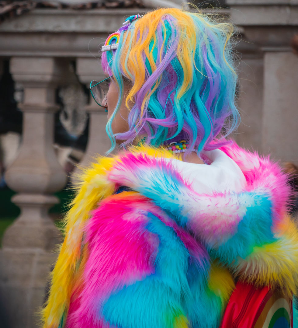 Bold, quirky, fascinating woman who recently endured a breakup with her significant other, beginning a new, exciting phase of life. Sporting colorful purple, yellow, and blue dyed hair, and wearing a faux fur rainbow coat with moxie.