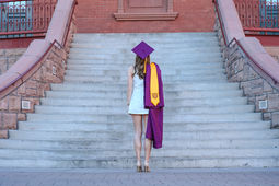 Female college graduate wearing cap and gown walking up the steps of an iconic college building