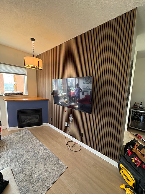 A complete living room transformation featuring floor-to-ceiling acoustic slat wall panels, carefully measured and cut around existing switches, outlets and the fireplace. The project also included TV mounting and custom-finished woodwork for the fireplace mantel.