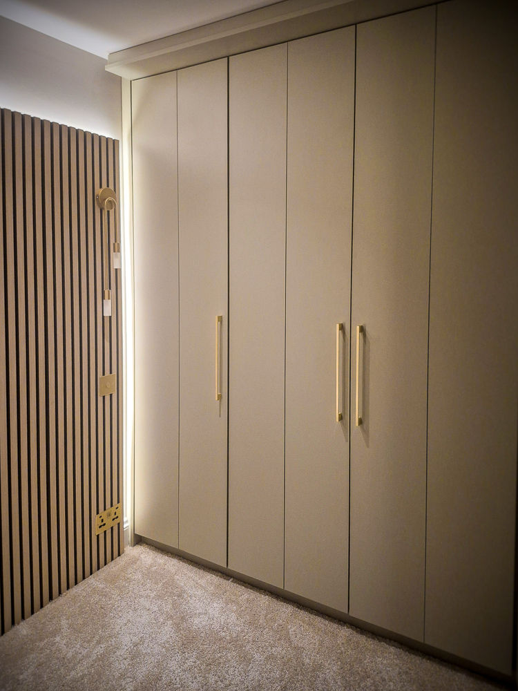Bespoke fitted wardrobe with bifolding doors and brass handles, handcrafted by Peter Hutchin Joinery in Hertfordshire and Essex.
