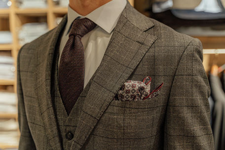 A close-up shot of a man wearing a brown, patterned three-piece suit with a dark tie and a coordinating pocket square.