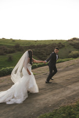 Bride and groom running hand in hand on green hillside at Terra Mia winter wedding on the Central Coast