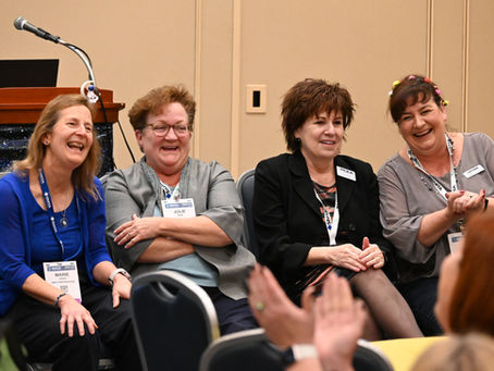 A group of enthusiastic women share a joyful moment while participating in a conference panel discussion, showcasing a lively exchange of ideas and camaraderie.