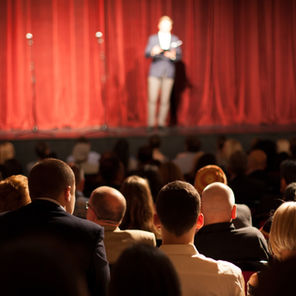 A lone person on stage in the distance with the backs of the large audience visible