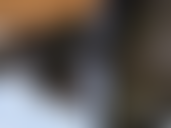 Icicles hang from a black downspout against a stone wall. Snow covers the ground, and the building's yellow trim adds contrast.