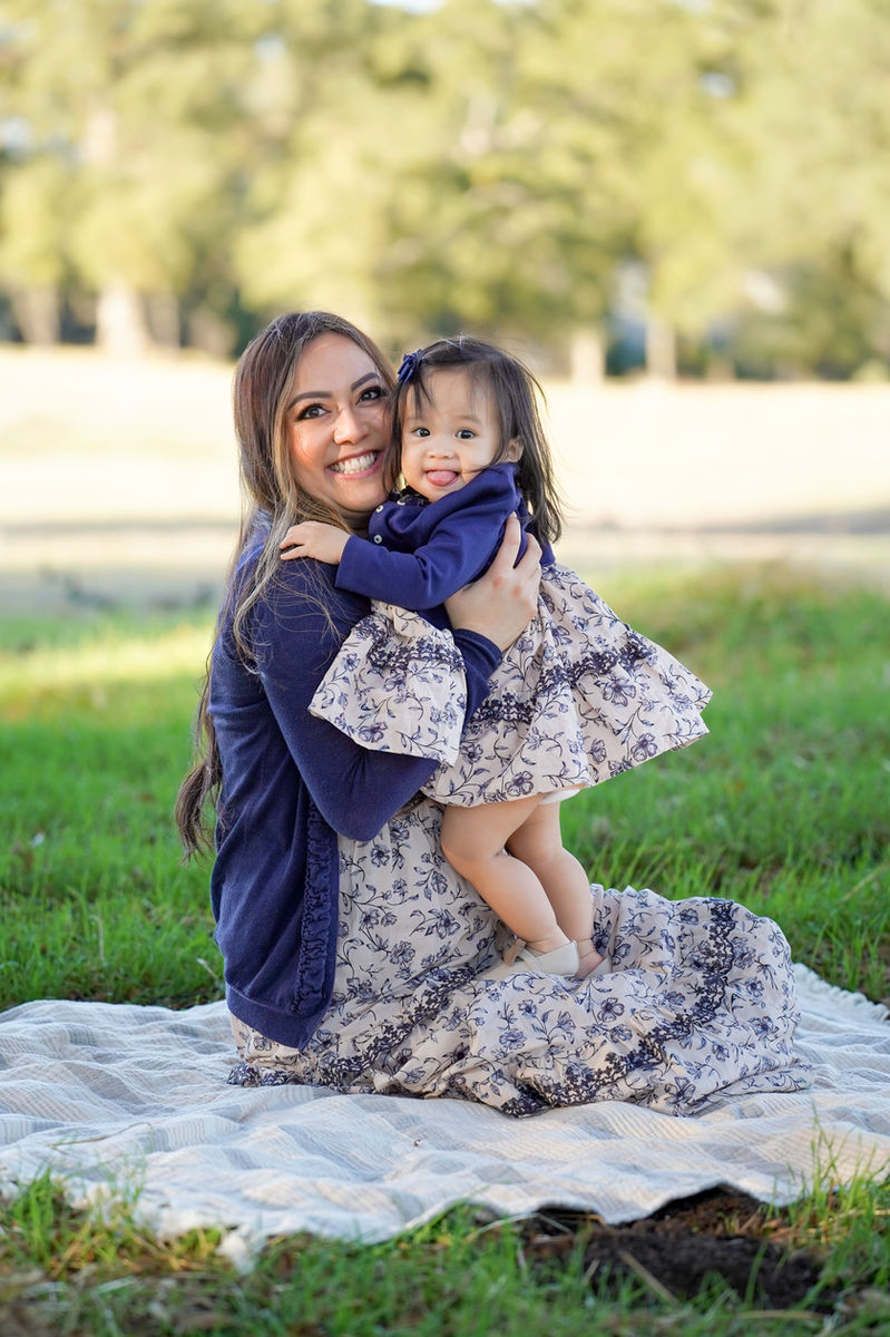 Mother in a navy floral dress holding her giggling toddler daughter on a soft picnic blanket during an on-location family session in the Sacramento area