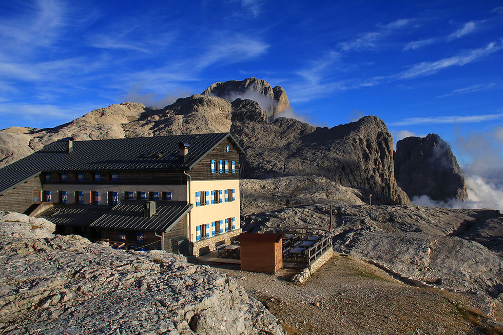 Rifugio Rosetta at the feet of Dolomite peaks in Italy with a strong blue sky and light high clouds.