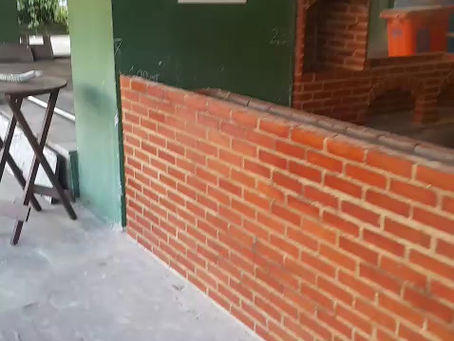 Churrasqueira vermelha livre sem parede atrás dela com bancada e balcões fechando a área gourmet do Condomínio em Senador Câmara.