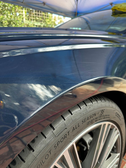Close-up of a blue Audi A5 undergoing paint correction. The surface reflects a glossy shine as a technician carefully polishes the car, highlighting the removal of scratches and imperfections.
