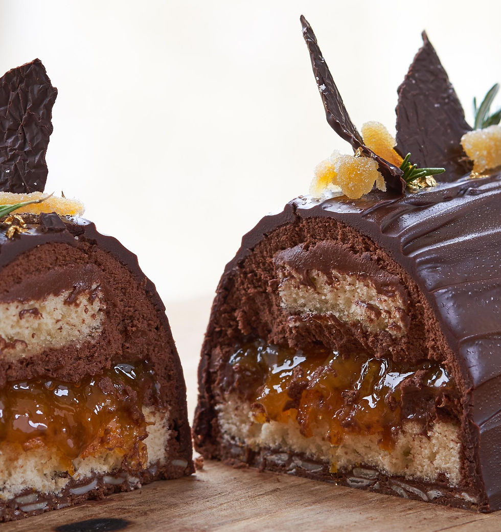Close-up of a sliced chocolate cake with creamy filling and orange jam. Topped with chocolate shards and sugared toppings on a wooden board.