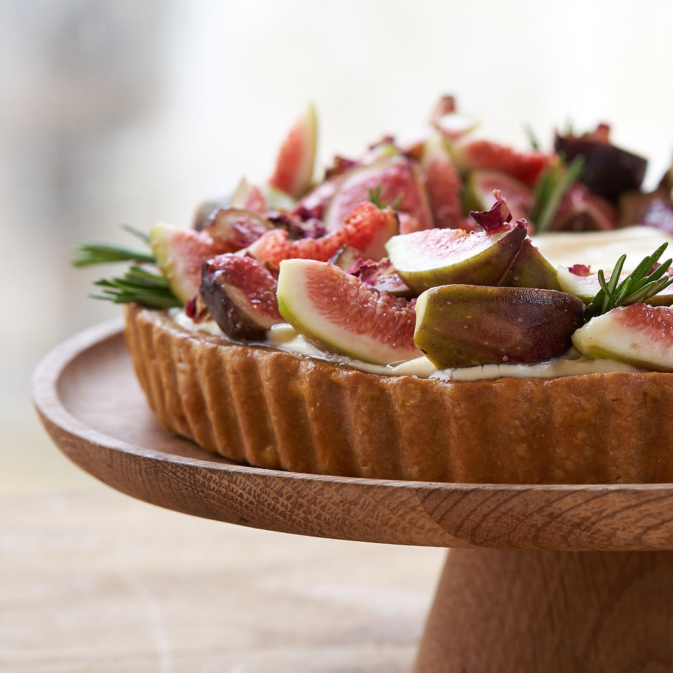 A fig tart topped with fresh figs and rosemary on a wooden stand. Background is blurred, creating a rustic, inviting atmosphere.
