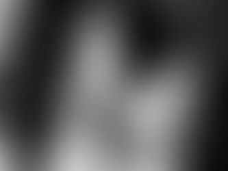 Woman in a white dress joyfully eats with a fork, smiling. Black and white image, indoor setting with blurred background.