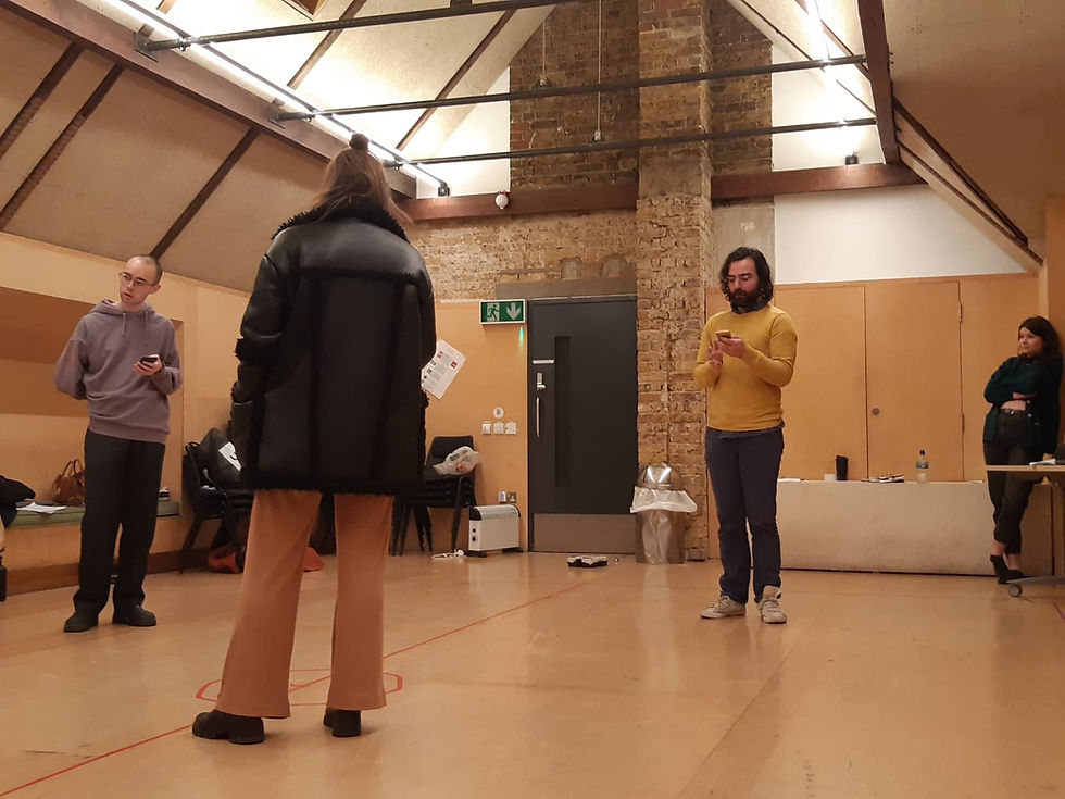 Four people standing in a bright rehearsal room, each with a phone in their hands.