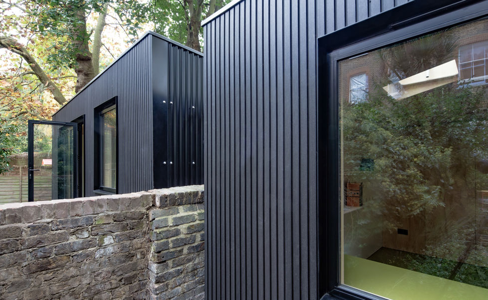 Side view of London garden room with black vertical cladding and stone wall.
