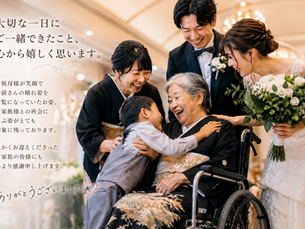 温かい光に包まれた結婚式場で、黒留袖を着た車椅子の高齢女性が孫の男の子に抱きつかれ、満面の笑顔を見せている。周囲には新郎新婦や家族が優しく見守り、再会の喜びにあふれた心温まるひとときが広がっている。