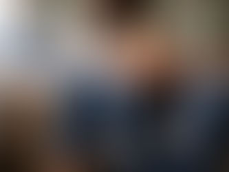 Adult tabby cat looking up at a ginger kitten being held by two people on a sofa, during an early introduction