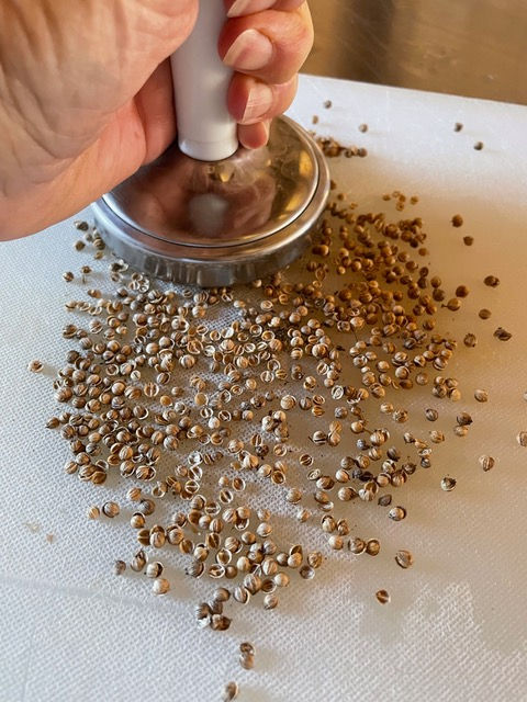 Crushing coriander seeds with a mallet.
