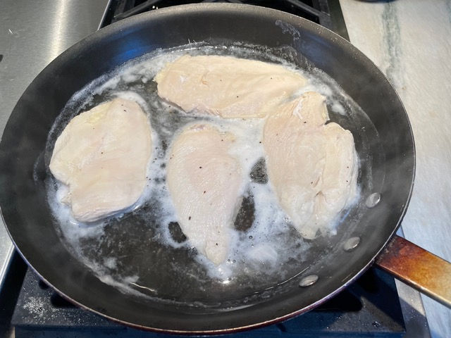 Poach chicken in simmering chicken stock and water.