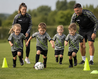 Four very young boys and girls smiling and running with a football through training cones during a Sturry Kings FC introductory mini-soccer session, with two coaches running playfully right behind them