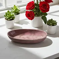 Red roses, succulents and a pink oval dish on a white table.