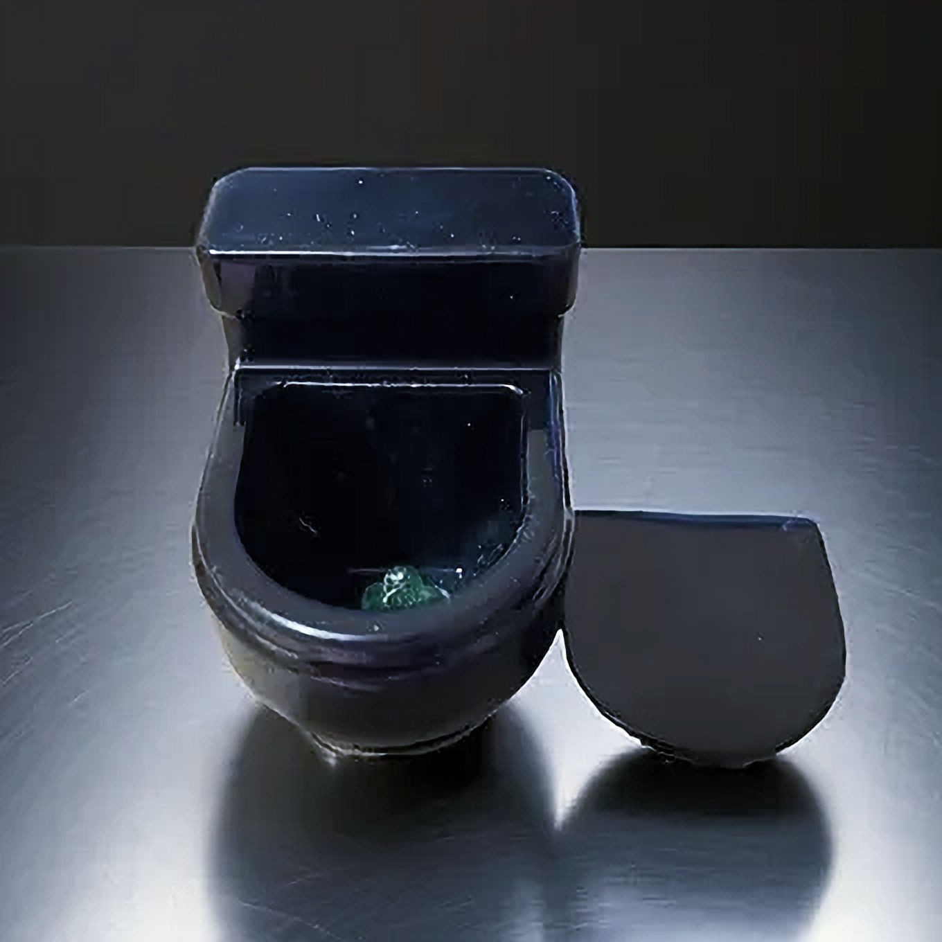 Miniature black toilet model with lid removed on dark background.