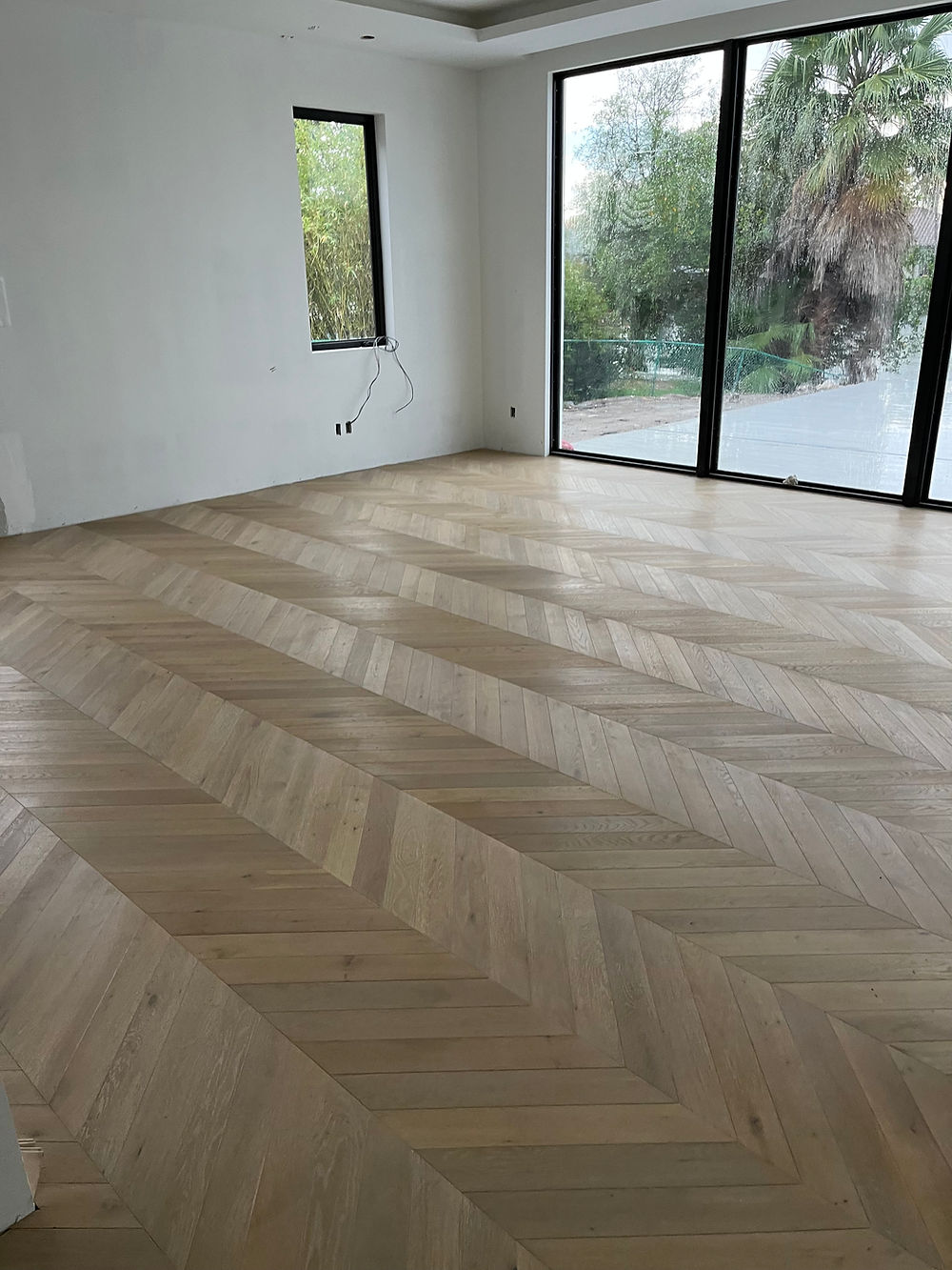 Upscale herringbone pattern light wood flooring installation in a modern home entryway.