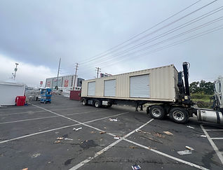 Loaded side-loader truck repositioning a shipping container in a paved parking lot for commercial transport.