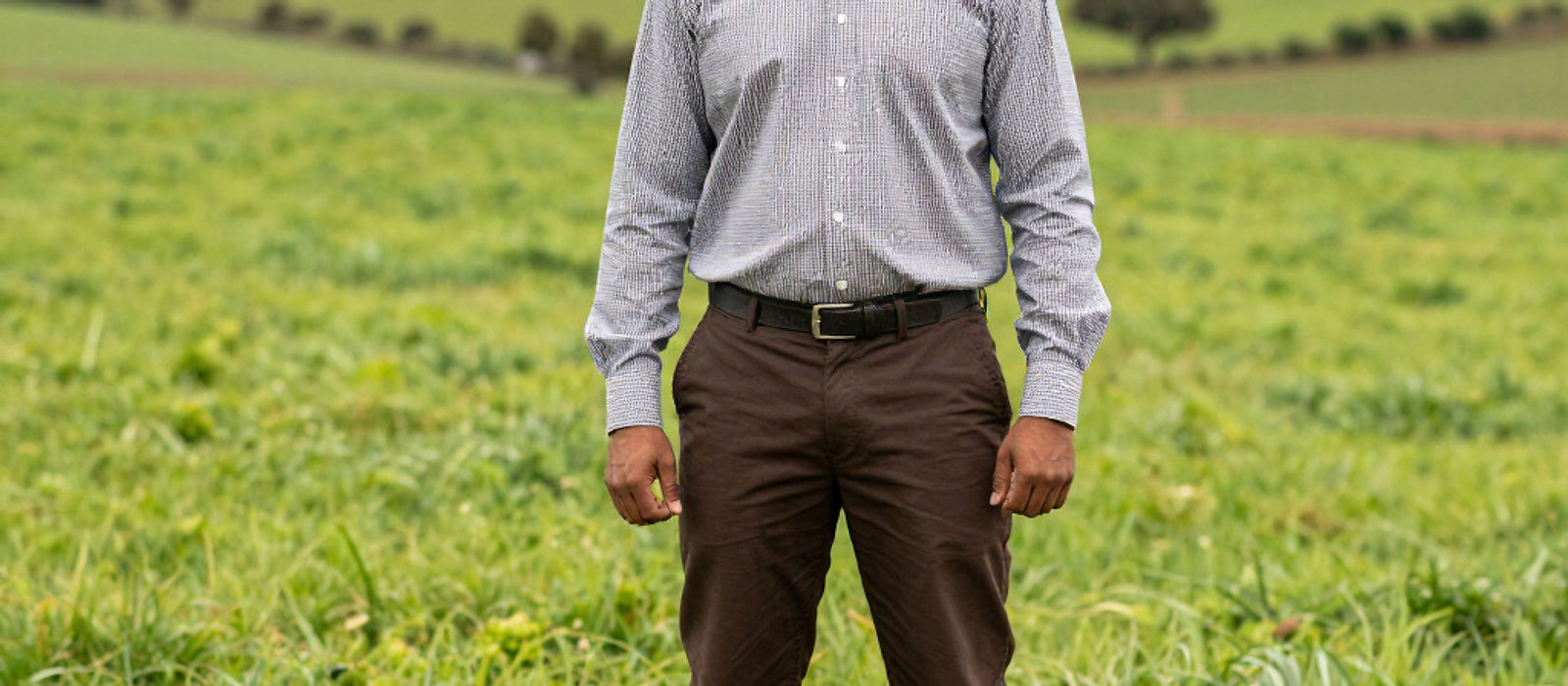 A farmer standing in a green paddock with rolling hills behind him