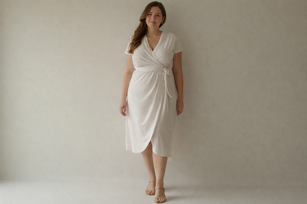 Mulher de vestido branco, em pé, sorri suavemente em fundo neutro. Atmosfera tranquila e elegante.