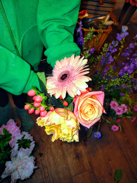 One of the Posy girls holding a bouquet of pink and yellow flowers with pops of greens and berry sprigs.