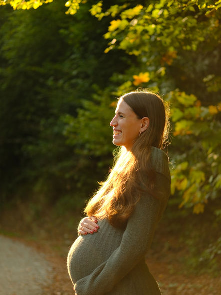 Ästhetische Schwangerschaftsfotografie einer werdenden Mutter im warmen Abendlicht im Wald – Porträt von Julia Mähl.