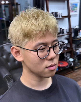 Side profile of a man with a platinum blonde textured crop haircut, soft layers, and modern barber styling.