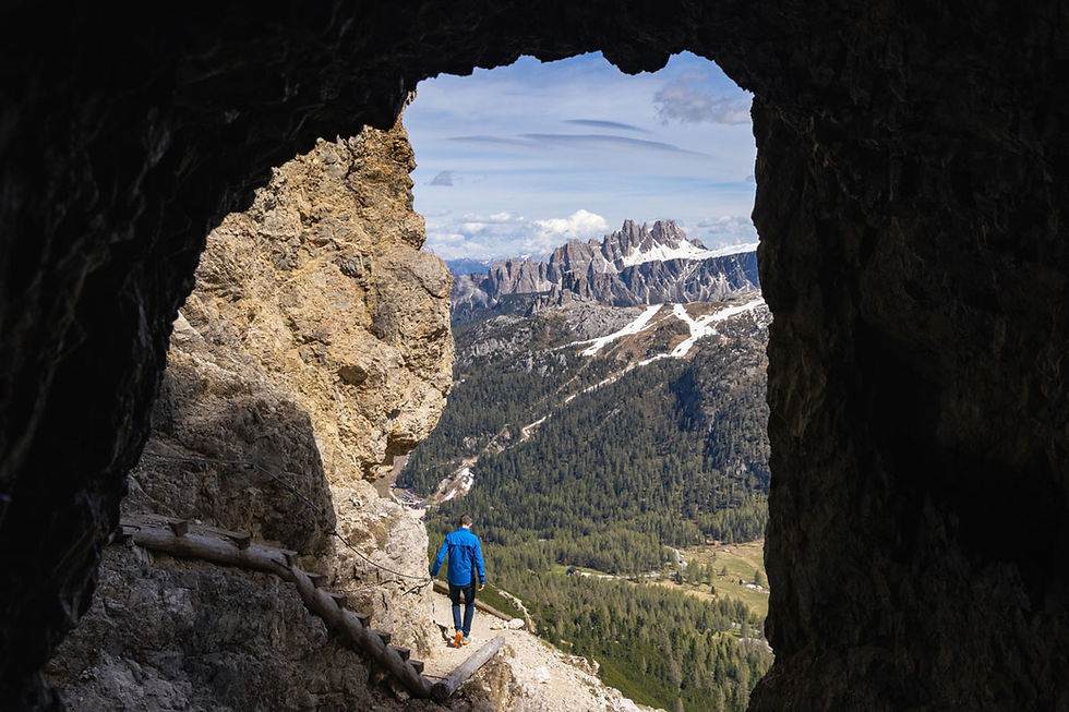A hiker examines the entrance of a narrow cave carved into a rocky cliff of the spectacular Lagazuoi tunnels.