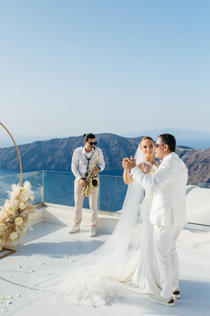 casal de noivos dançando na cerimonia em santorini, enquanto o saxofonista toca.