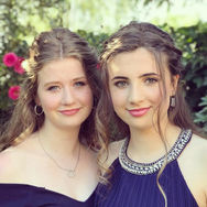Two young women pose, smiling with beautiful prom hair and makeup.